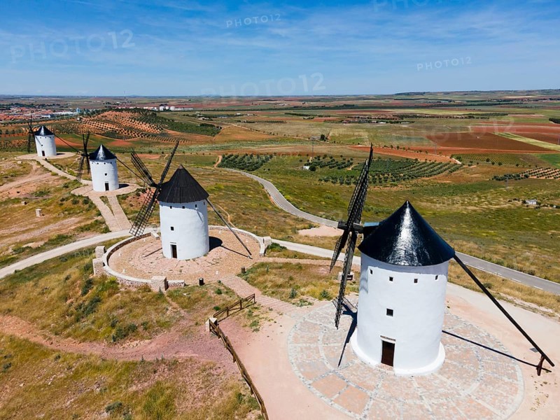 Four white windmills with black roofs on a wide hill under a clear blue sky and surrounded by fields, aerial view, Alcazar de San Juan, Ciudad Real, Castilla-La Mancha, Route of Don Quixote, Spain, Europe