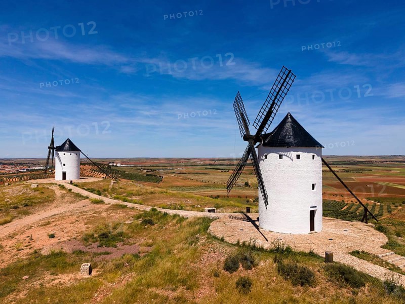 Two white windmills with black roofs in a vast landscape of fields under a sunny sky, aerial view, Alcazar de San Juan, Ciudad Real, Castilla-La Mancha, Route of Don Quixote, Spain, Europe