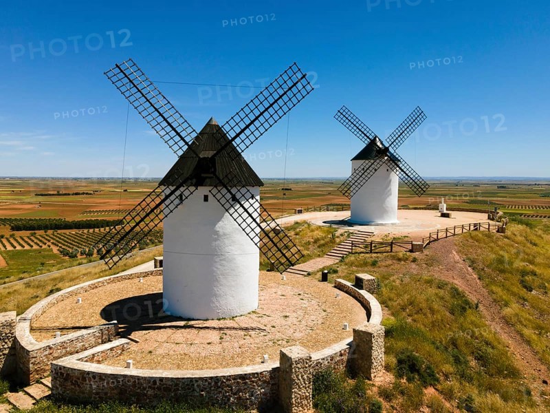 Two white windmills with black roofs on a hill surrounded by stone walls and wide fields, aerial view, Alcazar de San Juan, Ciudad Real, Castilla-La Mancha, Route of Don Quixote, Spain, Europe