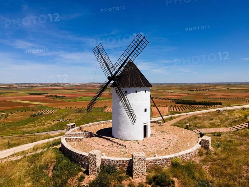 White windmill with black roof on a hill surrounded by stone walls and wide fields, aerial view, Alcazar de San Juan, Ciudad Real, Castilla-La Mancha, Route of Don Quixote, Spain, Europe