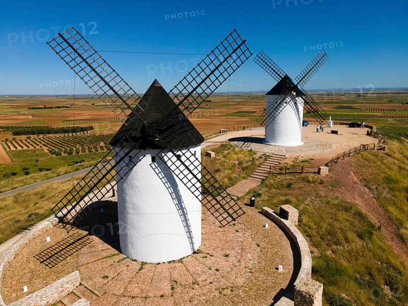 Two white windmills with black roofs in a wide field landscape in sunny weather, aerial view, Alcazar de San Juan, Ciudad Real, Castilla-La Mancha, Route of Don Quixote, Spain, Europe
