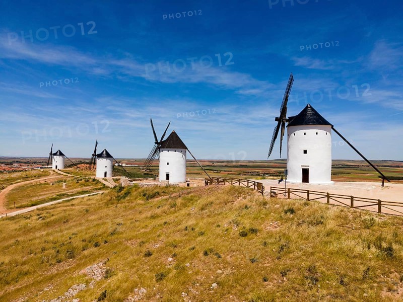 Several white windmills with black roofs in a vast scenic landscape under a clear blue sky, aerial view, Alcazar de San Juan, Ciudad Real, Castilla-La Mancha, Route of Don Quixote, Spain, Europe