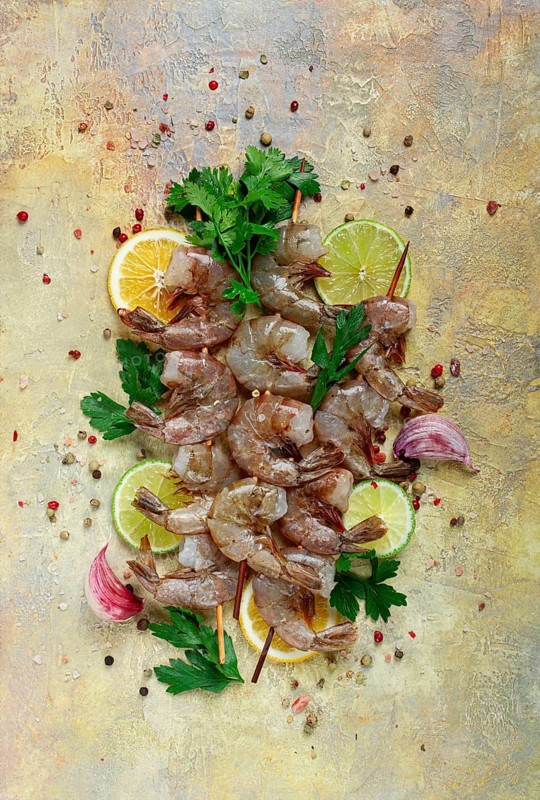 Raw shrimp on skewers, shrimp kebabs, slices of lime and lemon, spices and herbs, top view, without people
