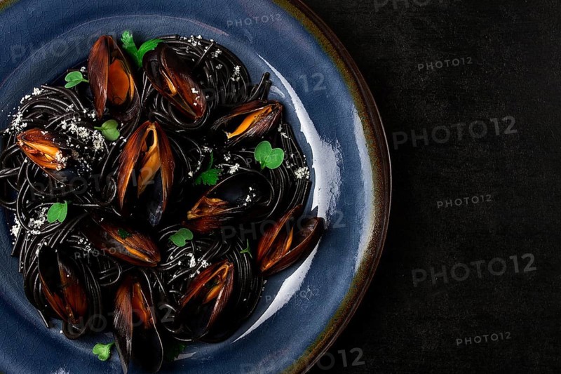 Spaghetti with black squid, black pasta, with boiled mussels, on a black plate, with parsley and parmesan cheese, close-up, selective focus, no people
