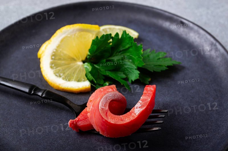 Chum salmon, cold smoked, on a fork, with lemon and parsley, top view, close-up, no people