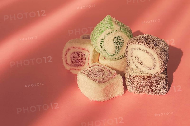Traditional Turkish delight, rols shape, in coconut flakes, on pink background, sunlight, horizontal, no people