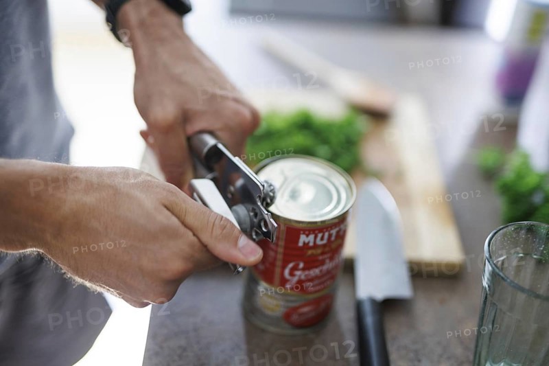Cooking topic. A man opens a tin of tomatoes. Berlin, 01.08.2024