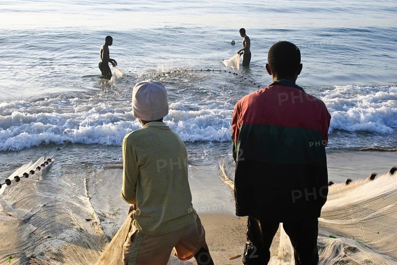 Boys are pulling a fishing net out of the water. Two fishermen are helping them. At Toamasina Madagascar