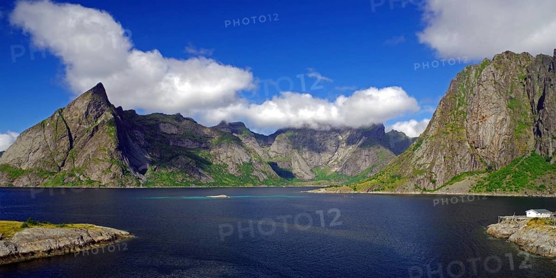 Impressive mountains under a blue sky with white clouds next to a calm fjord, Reinefjord, Hamnoy, Moskenes Lofoten, Nordland, Norway, Europe