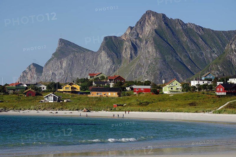 Small coastal village with colourful houses and beach, framed by majestic mountains under a clear sky, Ramberg, Flakstad, Flakstadoya, Lofoten, Nordland, Norway, Europe