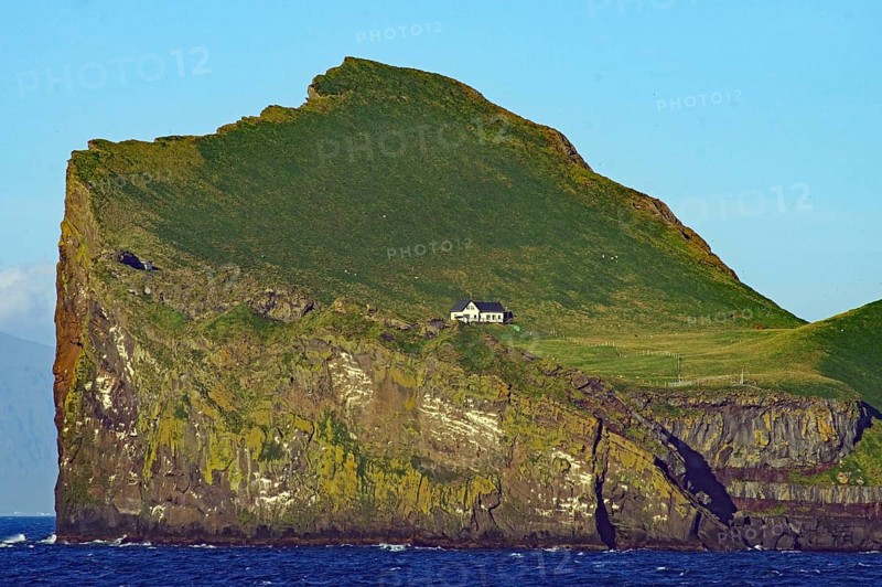 A small hut stands on a high, grassy cliff in the sea, Westman Islands, Iceland, Europe