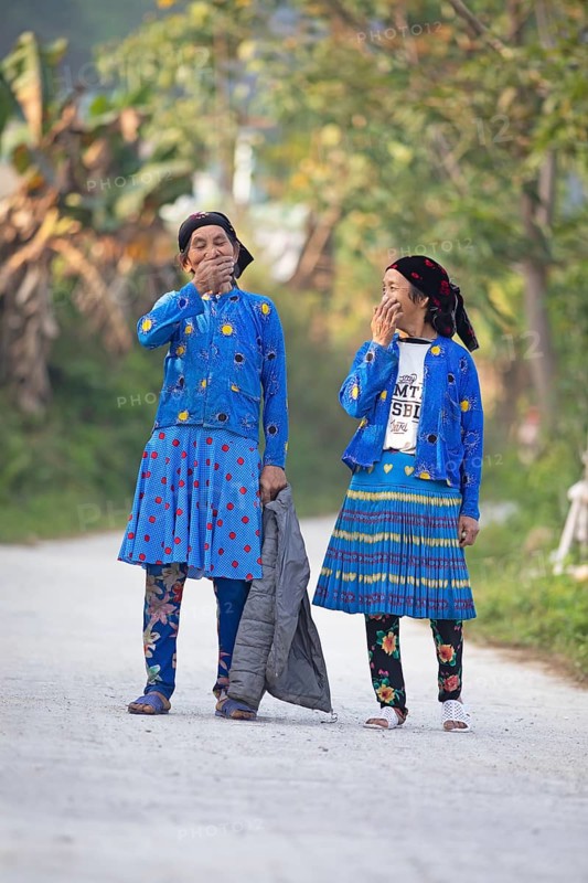 Two Hmong minority woman in everyday clothes stand on a street and cover their mouths with laughter, Du Gia, Ha Giang province, Vietnam, Asia