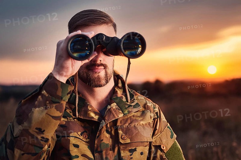 Man in camouflage clothing watches the sunset with binoculars in a quiet natural environment, AI generated, AI generated