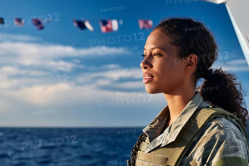 Woman in military uniform looking at the sea, with waving flags of the ship in the background, AI generated, AI generated
