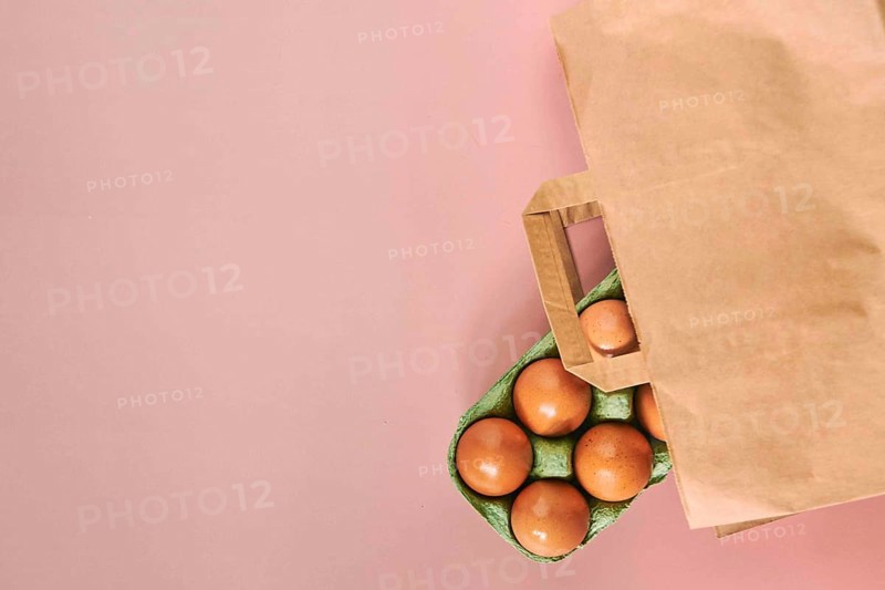 Kraft bag with chicken eggs in tray on beige background, shopping concept, space for text