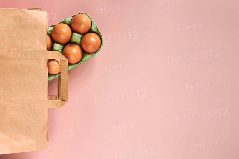 Kraft bag with chicken eggs in tray on beige background, shopping concept, space for text