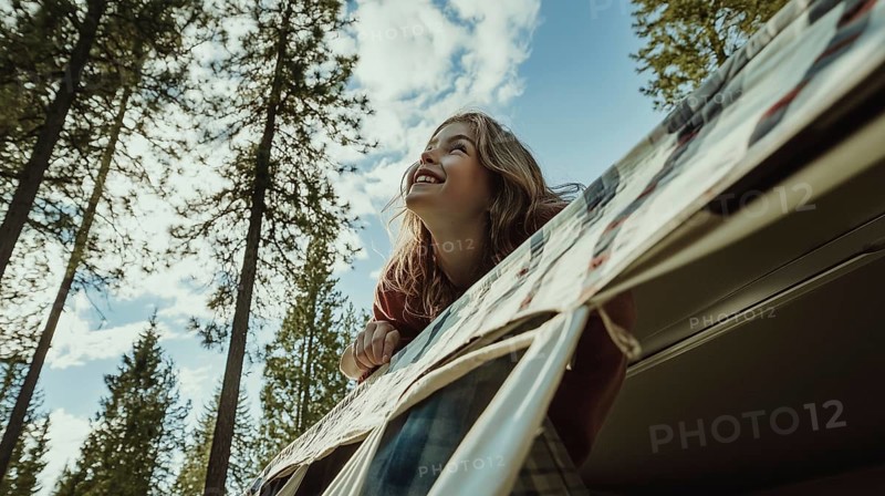 A smiling girl leaning out of a camper, looking up at the sky surrounded by tall trees, AI generated