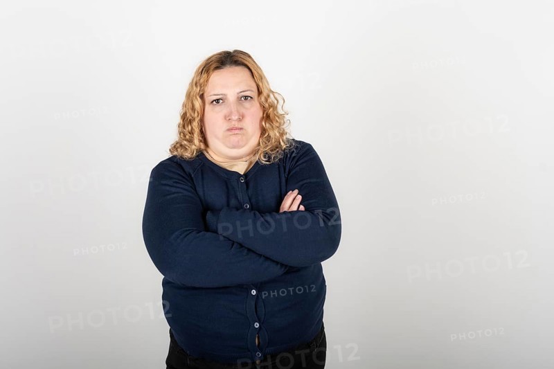 Portrait of plus size blonde woman with angry expression and arms crossed looking seriously at camera