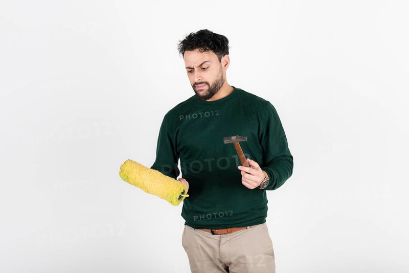Man looking confused at a paint roller and hammer