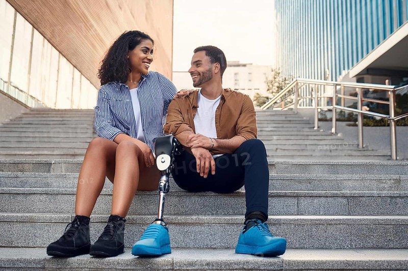 Couple, man with prosthetic leg, sitting on the steps in the city, the woman laughs at her partner with prosthetic leg, ai generated, AI generated