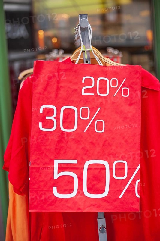 Red sign discount on a shopping bag in front of a clothing rack with t-shirts and shop window, Germany, Europe