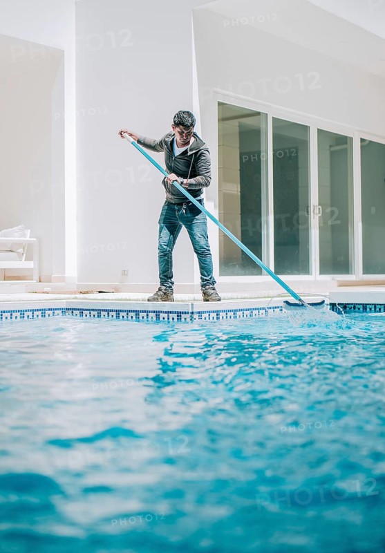 Home pool cleaning with wall brush. Male worker cleaning a home swimming pool with special brush