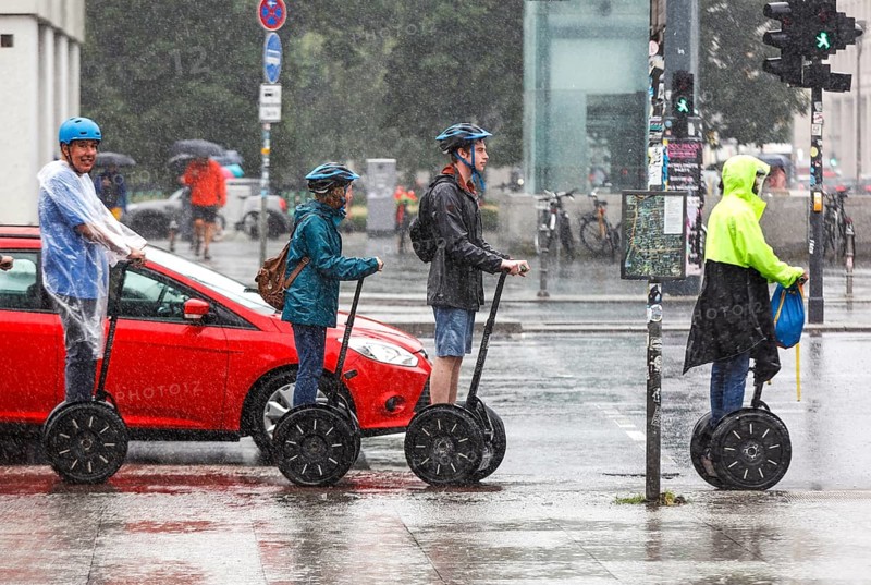 Tourists standing at a traffic light in heavy rain with Segway personal transporters, Berlin, 23 06 2023