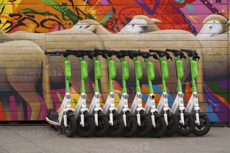 Several parked electric scooters in the bike rental of the company Lime, OnLime and Uber, behind it construction fence with sheep, flock of sheep, graffiti, Frankfurt am Main, Hesse, Germany, Europe