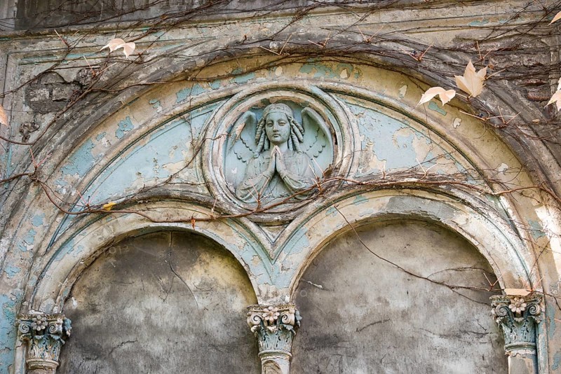 Relief of an angel on a dilapidated blue façade, historical angel, praying, tomb with round arches and columns in the cemeteries on BergmannstraÃŸe, vines with autumn leaves, symbolic image of transience, Berlin-Kreuzberg, Berlin, Germany, Europe