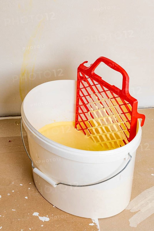 Scraper grid in bucket with yellow wall paint, painting work