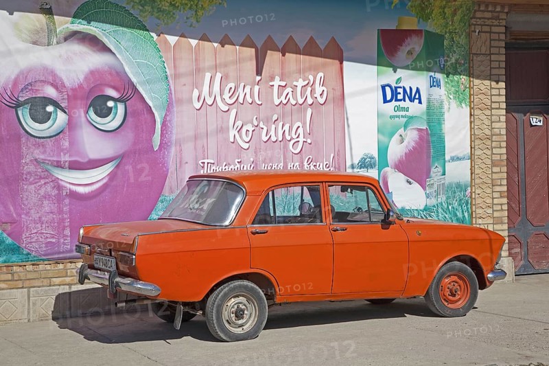 Old Trabant parked in front of advertisement painted on wall in Uzbekistan