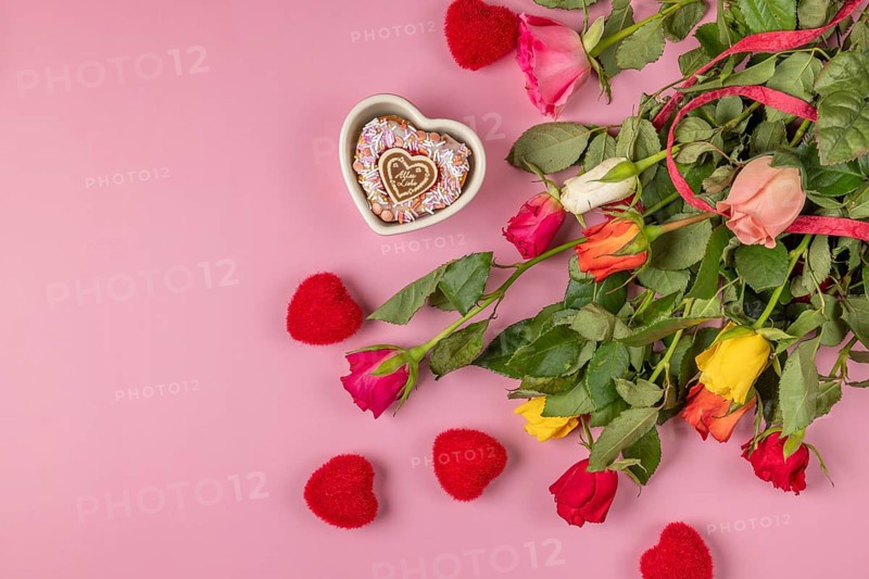 Colourful bouquet of roses with red hearts and heart-shaped bowl with muffin on a pink background