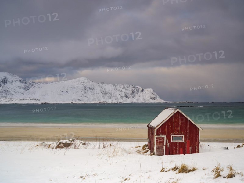Red Rorbuer fisherman's hut on the beach in the snow, snow-covered mountains behind, Ramberg, Flakstadoya, Lofoten, Norway, Europe