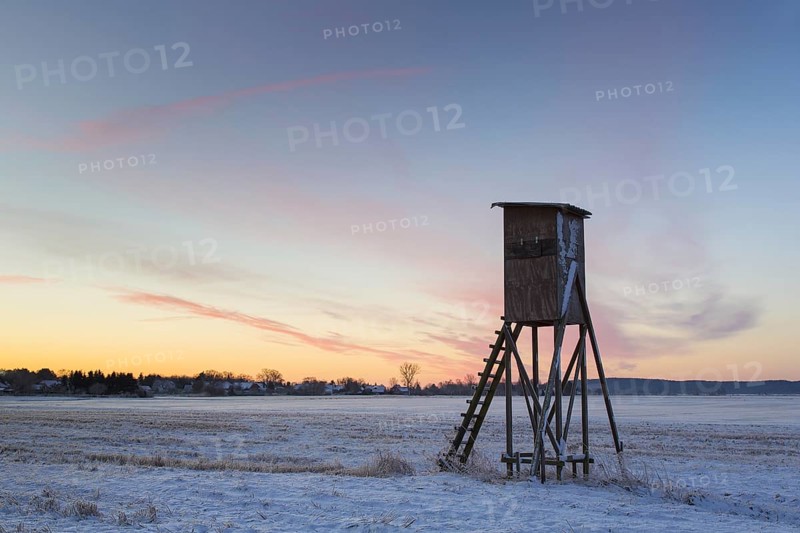Raised hide for hunting roe deer at sunrise in snow covered field in winter, Lower Saxony, Germany, Europe