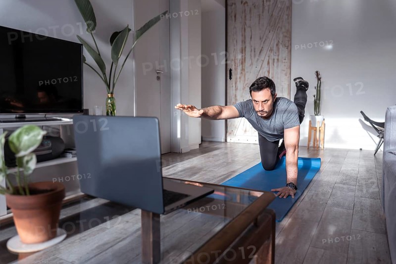 Latino personal trainer in online class, concentrating on the laptop. Work at home online. Healthy lifestyle, sport and technology