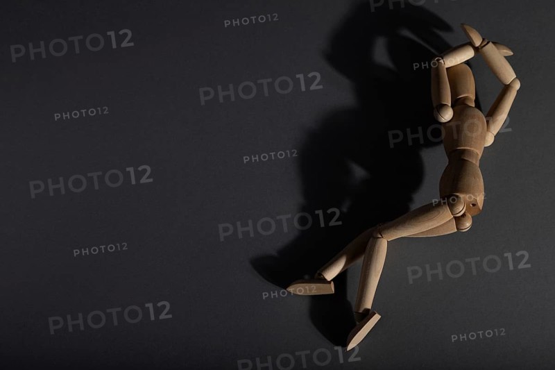 Wooden mannequin lies in a protective position on gray background. loneliness, violence, vulnerability, depression disorder concept. copy space, hard light