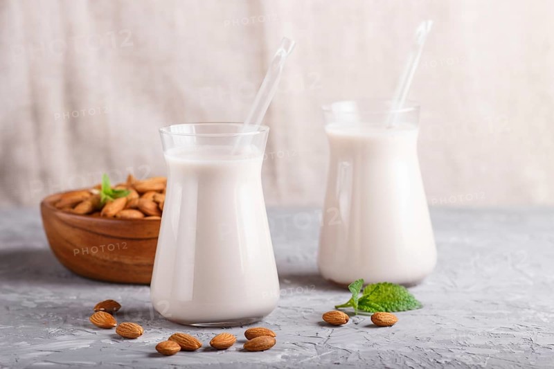 Organic non dairy almond milk in glass and wooden plate with almond nuts on a gray concrete background. Vegan healthy food concept, close up, side view
