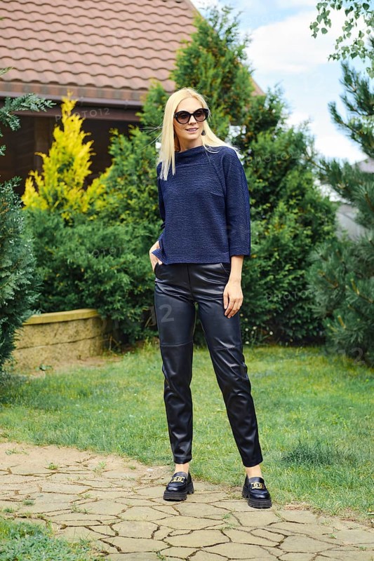 Cheerful woman in knitted blouse and leather trousers in the pathway of the garden