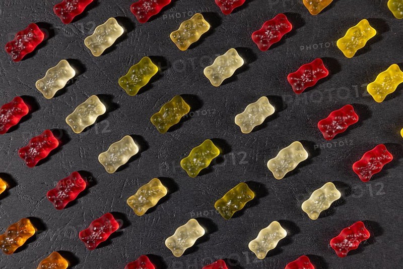 Different coloured gummy bears in rows, on a dark background
