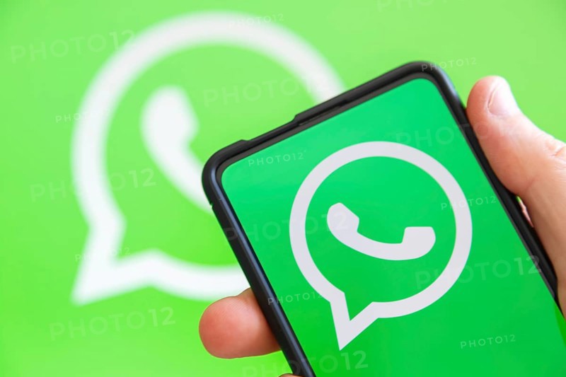 Hand holding mobile phone with WhatsApp logo messenger app computer screen