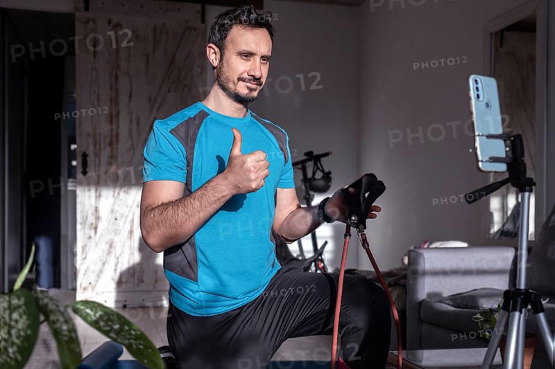 Attractive latin man personal trainer recording with phone content for online fitness business. Freelance filming online training program with virtual workout and exercises for social media