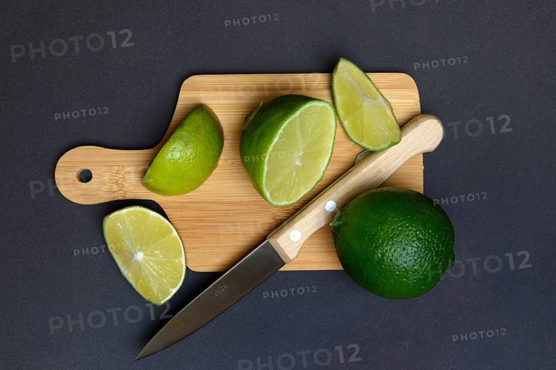 Halved limes on a chopping board with a kitchen knife