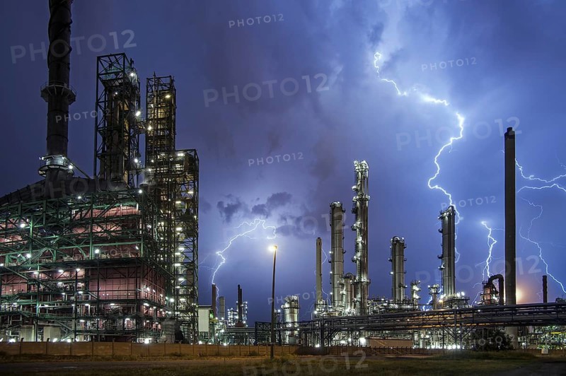 Lightning bolts striking over oil refinery at industrial estate during heavy thunderstorm at night, conceptual picture for global warming due to carbon dioxide emissions