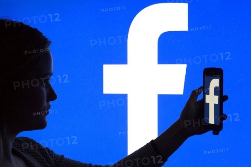 Silhouette of a woman with a smartphone in her hand in front of a Facebook logo, 12/01/2016