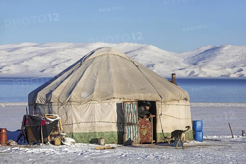 Kyrgyz man in door opening of traditional yurt in the snow along Song Kul, Song Kol lake in the Tian Shan Mountains, Naryn Province, Kyrgyzstan, Asia