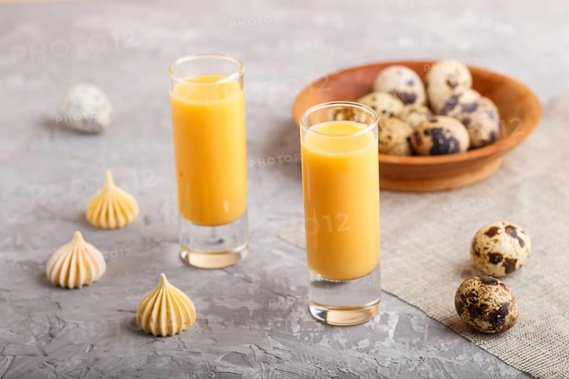 Sweet egg liqueur in glass with quail eggs and meringues on a gray concrete background. Side view, close up