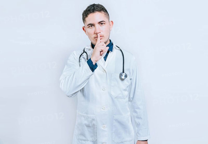 Doctor making silence gesture on white background. Latin doctor silencing and looking at the camera