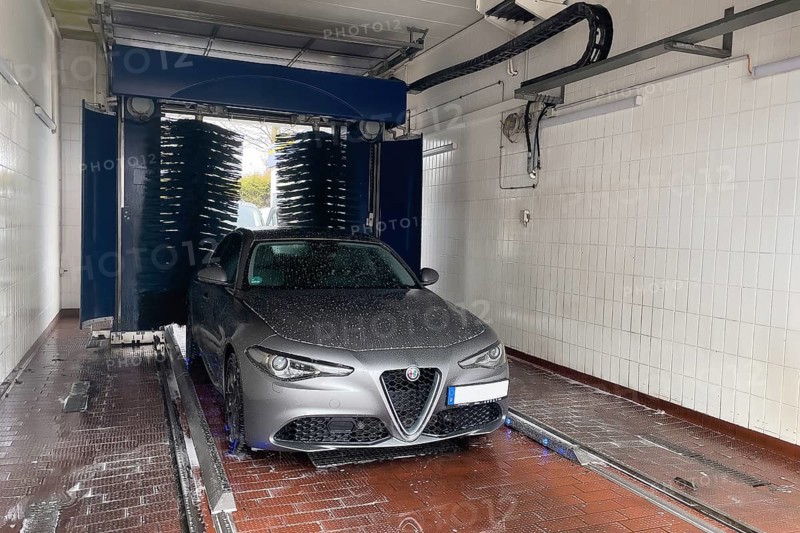 Front view of motor vehicle sporty sedan Italian make automobile Alfa Romeo Giulia being sprayed in car wash with car shampoo chemical care chemicals, rotating brushes in background, car care, Germany, Europe
