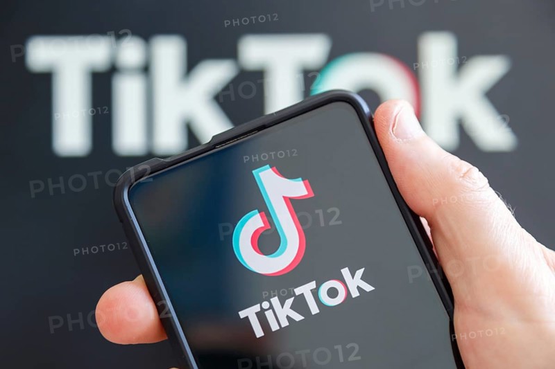 Hand holding mobile phone with TikTok logo social media with computer screen