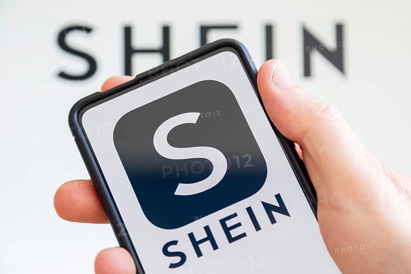 Hand holding mobile phone with Shein logo online marketplace online trading ecommerce computer screen